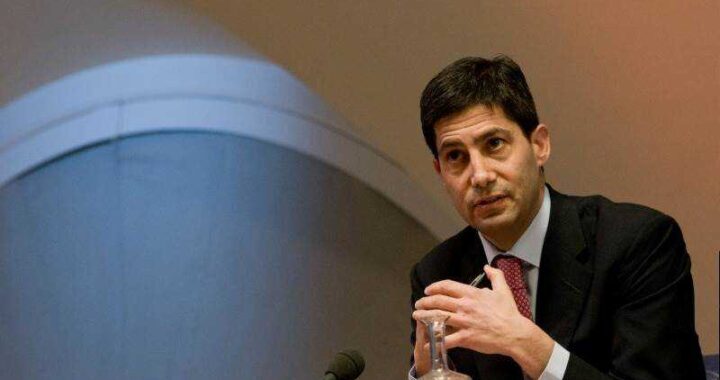 Kevin Warsh en rueda de prensa como nuevo presidente de la Fed con gráficos de inflación y tipos de interés al fondo