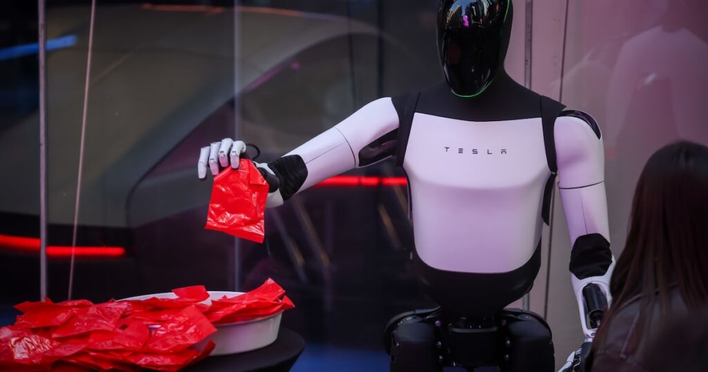 Prototipo del robot Optimus de Tesla en una fábrica, mostrando su diseño bípedo y sensores de IA para 2027