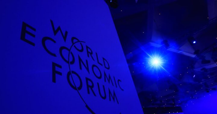 Ejecutivo analizando gráficos de inversión en IA durante el Foro de Davos 2026 con datos de OpenAI y Anthropic en pantallas