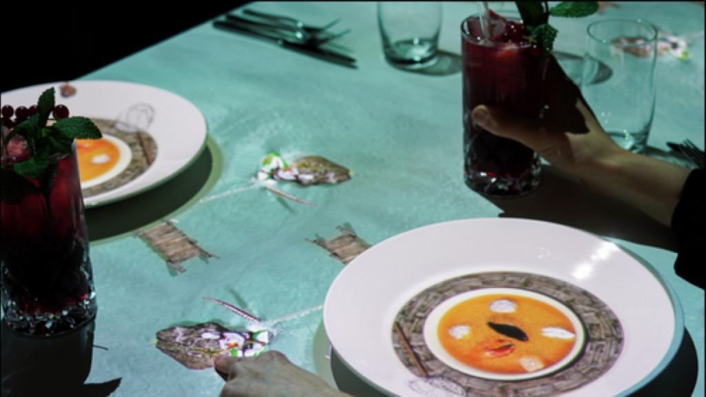 Proyección 3D del chef animado de 6 cm cocinando sobre una mesa en Quito con platos reales sincronizados