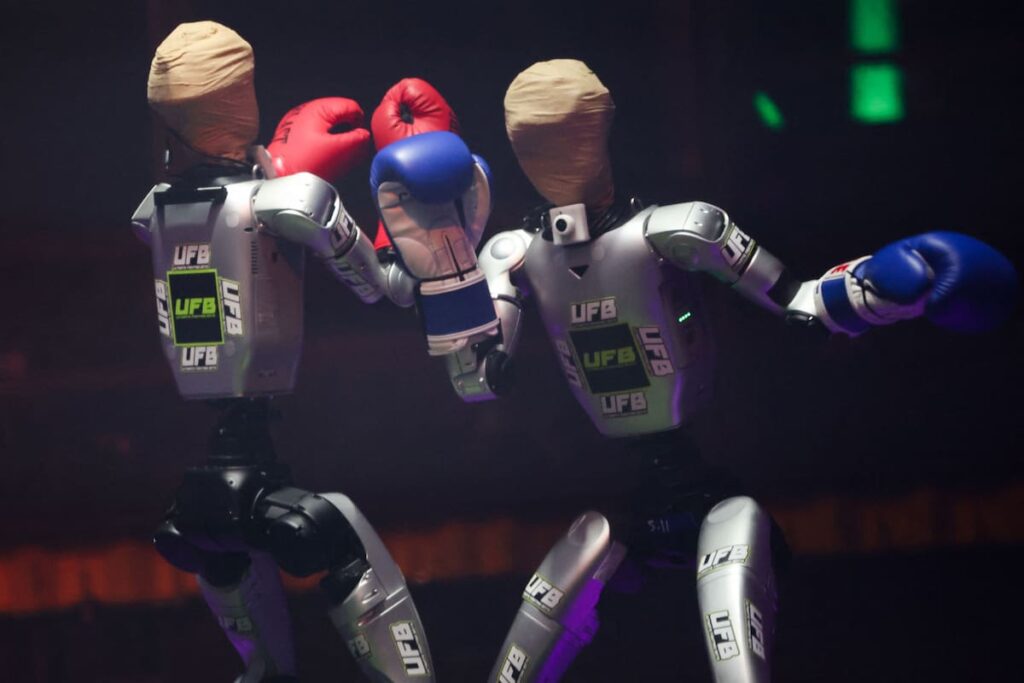 Dos robots humanoides midiendo fuerzas en un ring futurista durante combate en vivo con pilotos controlándolos