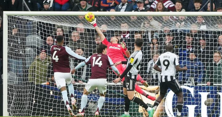 Dibu Martínez en acción con guantes amarillos deteniendo un remate en el St. James Park durante el Newcastle vs Aston Villa
