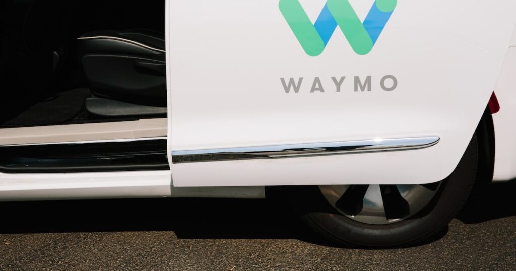 Vehículo autónomo de Waymo circulando por calles de Miami sin conductor, con sensores LiDAR visibles y rascacielos de fondo