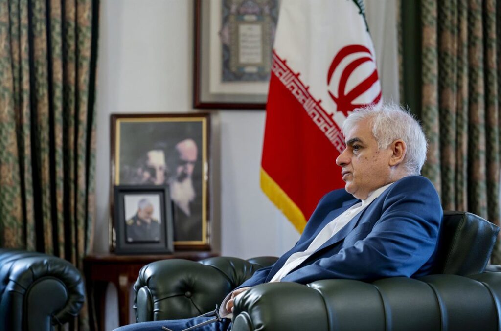 Embajador iraní en entrevista tensa con mapa de Oriente Medio y bandera de Irán al fondo