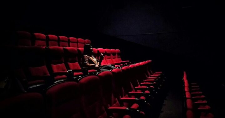 Multitud en concierto con luces brillantes mientras sala de cine vacía muestra carteles de 'últimas funciones'