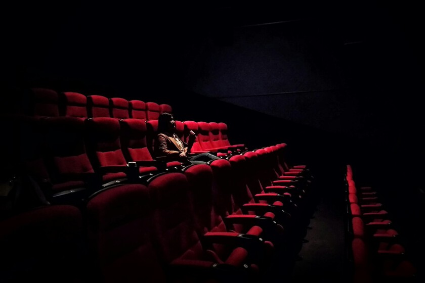 Multitud en concierto con luces brillantes mientras sala de cine vacía muestra carteles de 'últimas funciones'