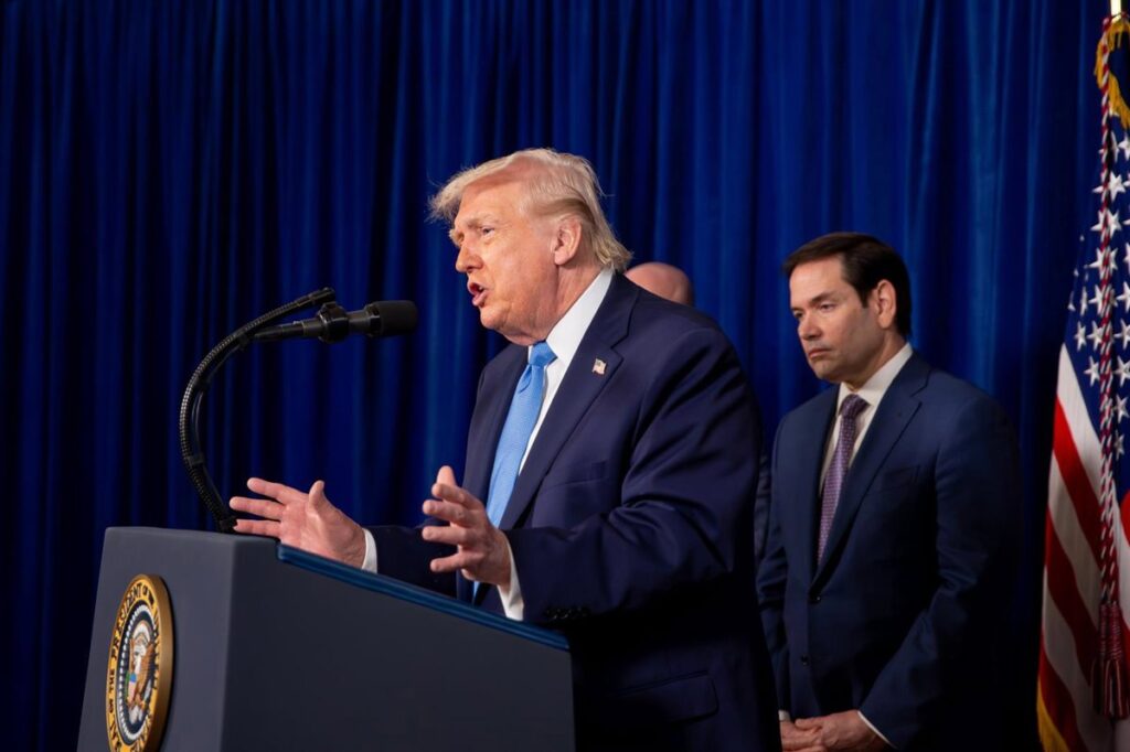 Donald Trump firma documento con bandera de EE.UU. y gráfico de arancel del 25% sobre productos de Irán en fondo
