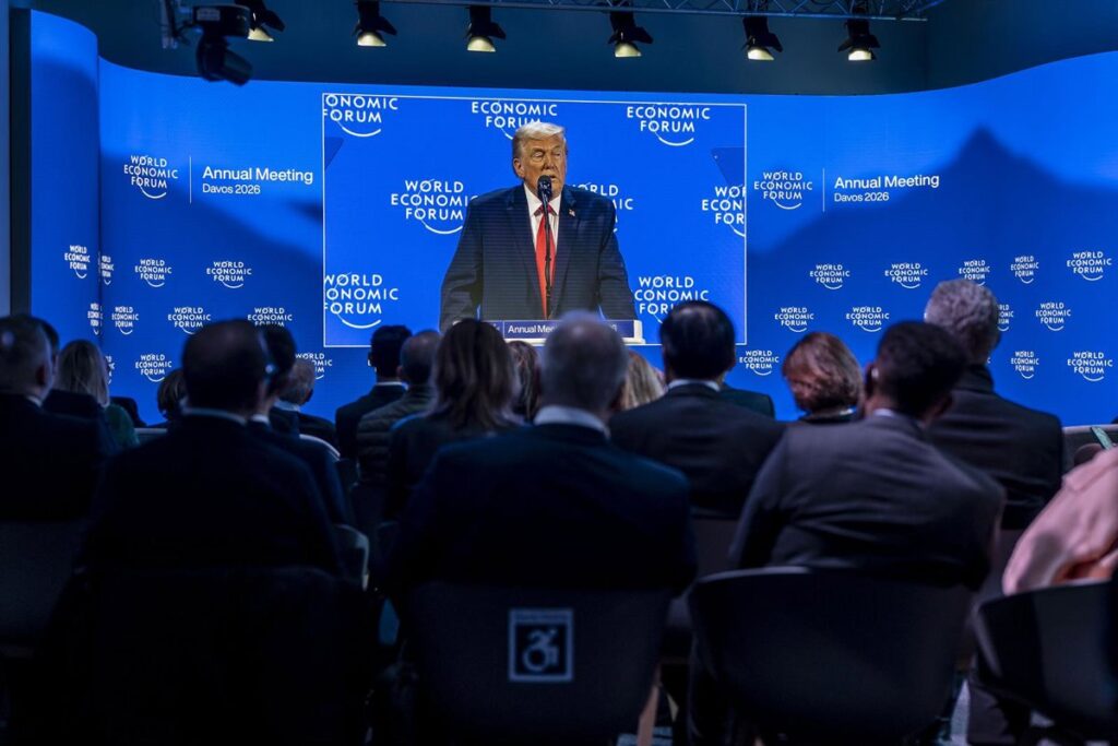 Donald Trump en Davos 2024 mostrando gráficos de crecimiento económico de EE.UU. vs Europa con expresión triunfal