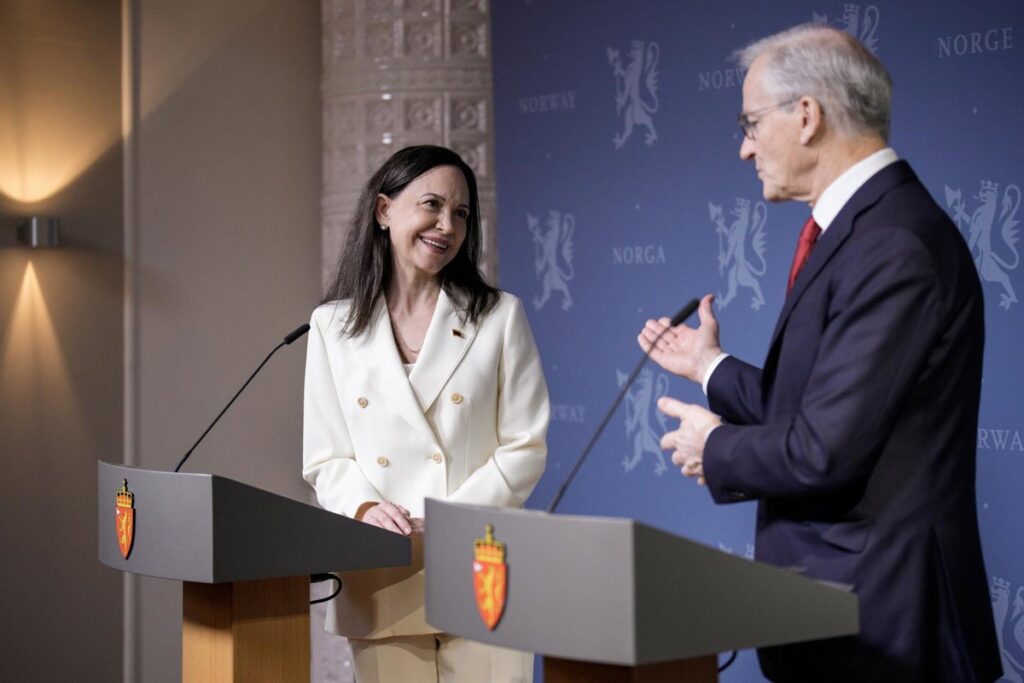 María Corina Machado con medalla del Nobel de la Paz 2025 frente a bandera de Venezuela en tensión geopolítica