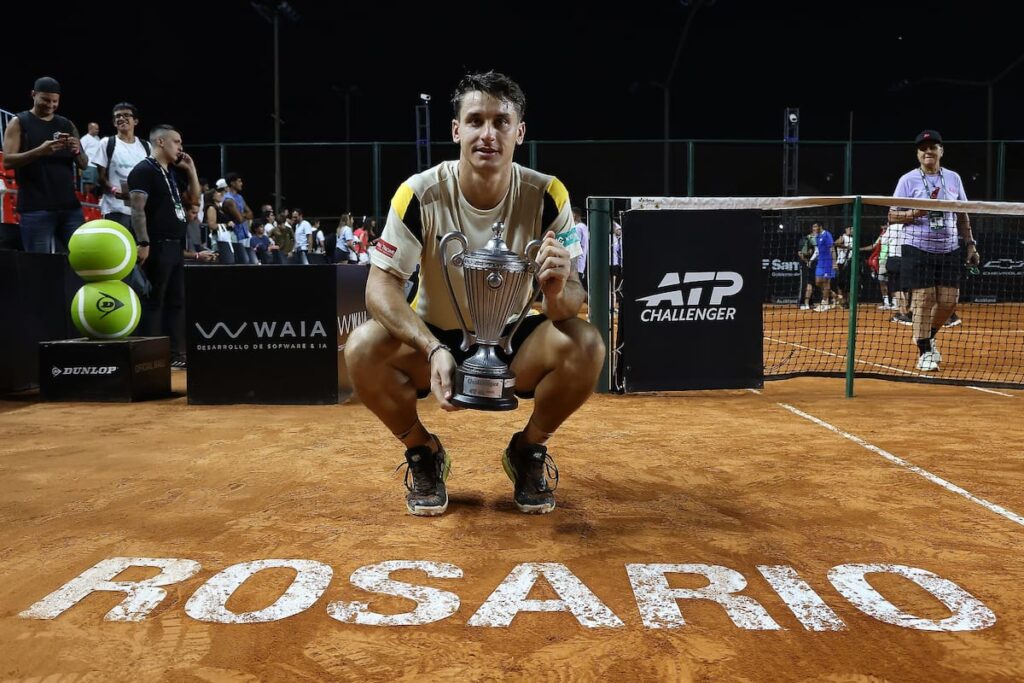 Camilo Carabelli celebra su bicampeonato en Rosario Challenger con el trofeo en alto, fondo de canchas de polvo de ladrillo