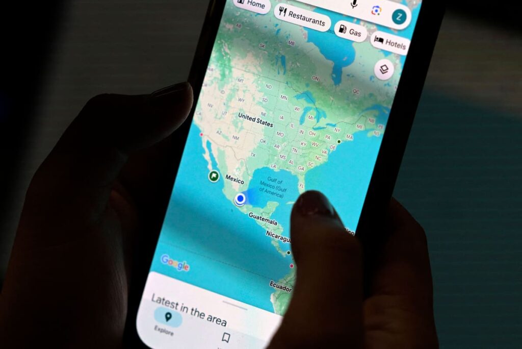 Pantalla de smartphone mostrando el punto azul de Google Maps con círculo de error en zona urbana con rascacielos