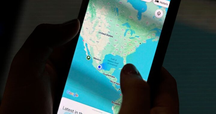 Pantalla de smartphone mostrando el punto azul de Google Maps con círculo de error en zona urbana con rascacielos