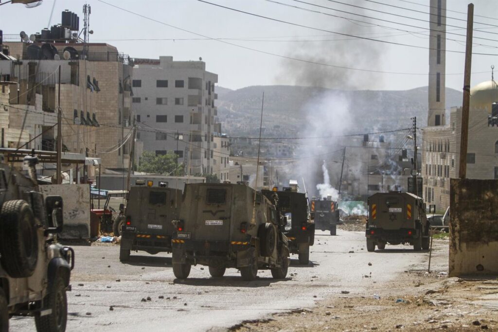 Manifestantes palestinos en Jericó durante operación militar israelí con soldados armados al fondo