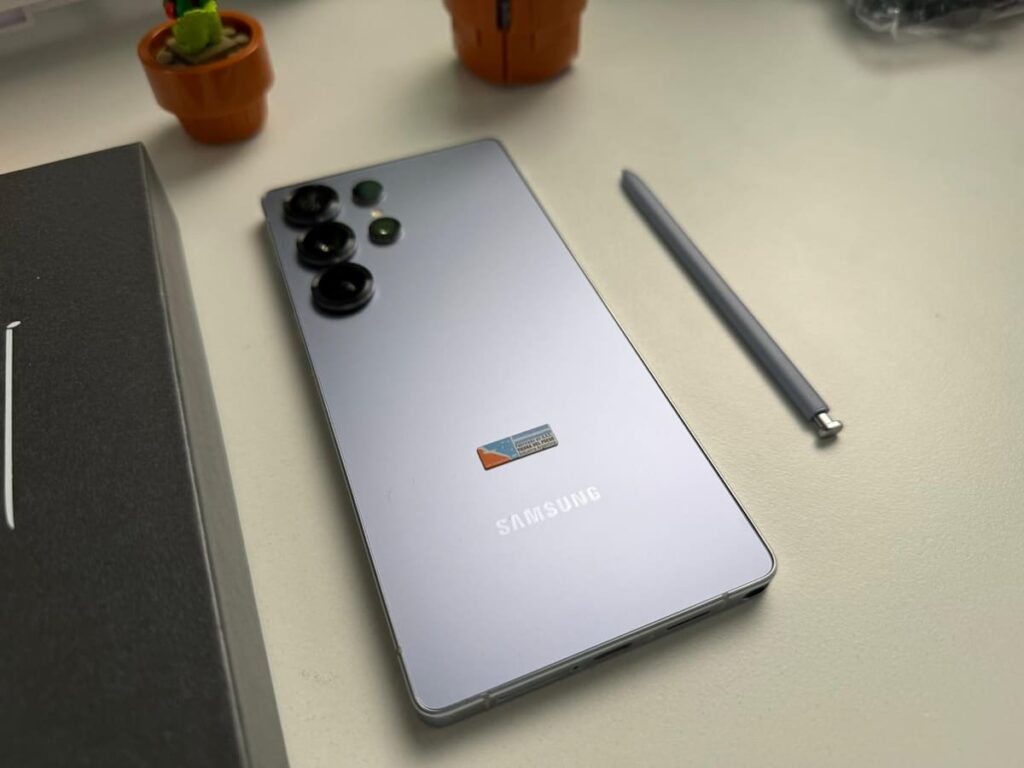 Prototipo del Samsung Galaxy S26 mostrando su pantalla con interfaz de IA y logo de Galaxy Unpacked 2025