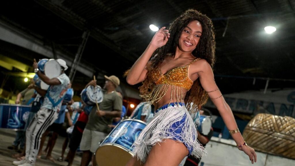 Bailarines de escuela de samba ensayan en galpón con paredes agrietadas, simbolizando la exclusión en el Carnaval de Río