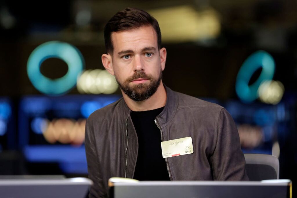 Jack Dorsey en conferencia anunciando despidos masivos por IA con gráficos de acciones en alza al 27%