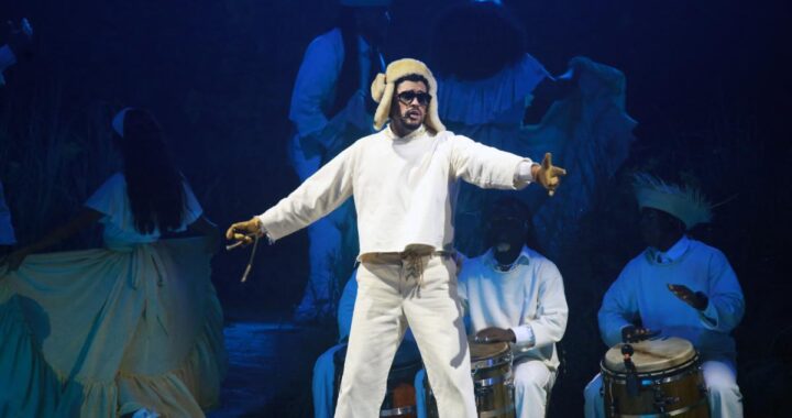 Bad Bunny en el escenario del Super Bowl LX con micrófono y luces de fondo, desafiando con su música