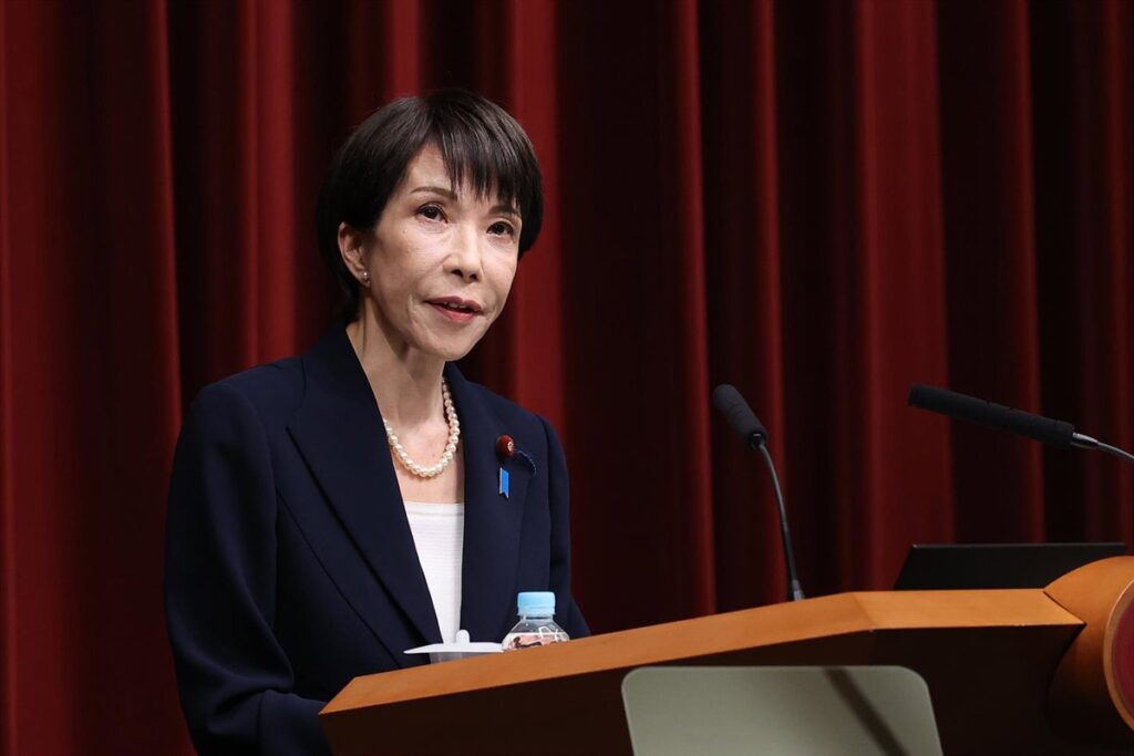 Sanae Takaichi en mitin con bandera de Japón y gráficos de gasto militar en pantalla gigante, reflejo de su apuesta por el rearme antes del 8F