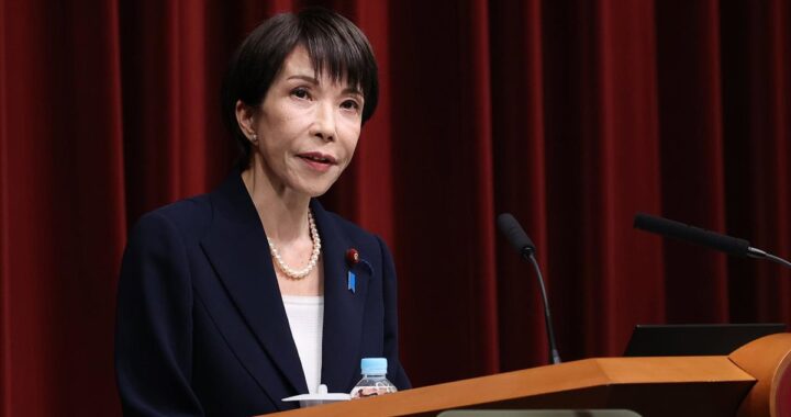 Sanae Takaichi en mitin con bandera de Japón y gráficos de gasto militar en pantalla gigante, reflejo de su apuesta por el rearme antes del 8F