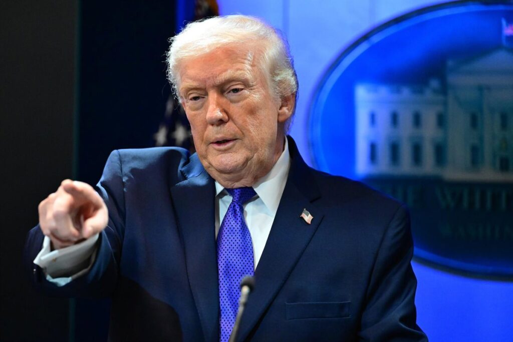 Donald Trump firma documento con gráficos de aranceles al 15% y caída de bolsa en pantallas de fondo