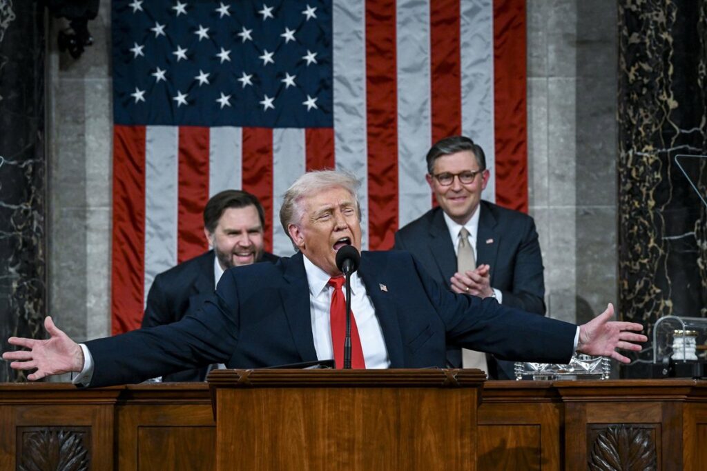 Donald Trump señalando con gesto airado durante discurso en el Congreso, con cartel de protesta 'Las personas negras no son simios' al fondo