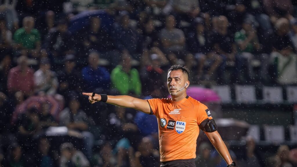 Árbitro Lobo Medina muestra tarjeta roja a jugador de Banfield bajo lluvia intensa y mirada de hinchas