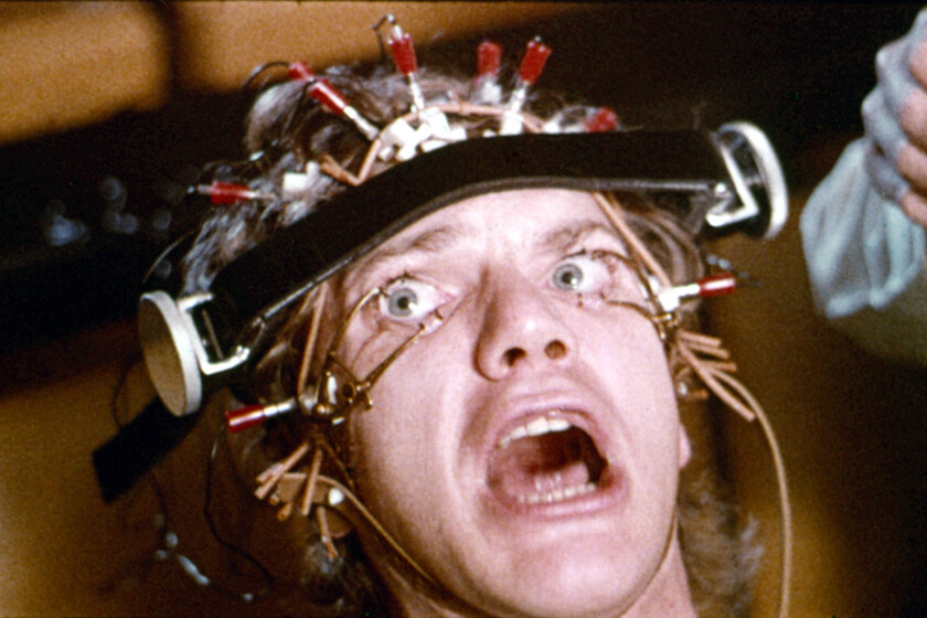 Primer plano de Malcolm McDowell con los ojos forzados abiertos en la escena de terapia de 'La Naranja Mecánica', mostrando el dispositivo que le causó lesiones reales