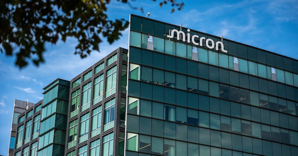 Gráfico de caída de acciones de Micron frente al logo de SK Hynix con fondo de Wall Street y chips HBM en primer plano