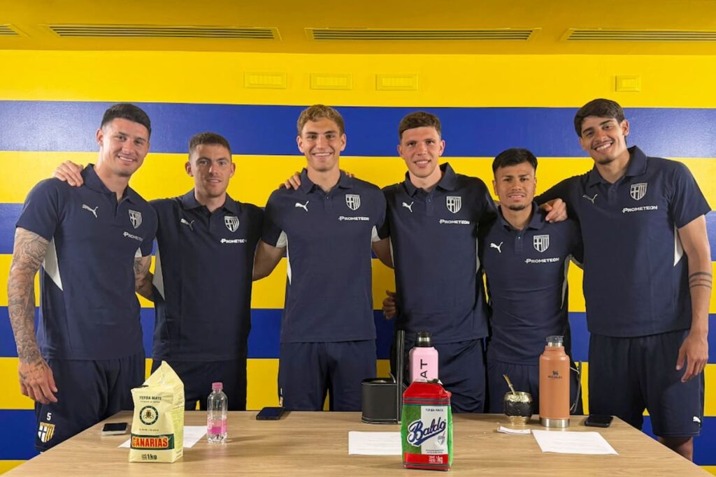 Grupo de 6 futbolistas argentinos de Parma sonriendo con camisetas del club y mate en mano en el estadio Tardini