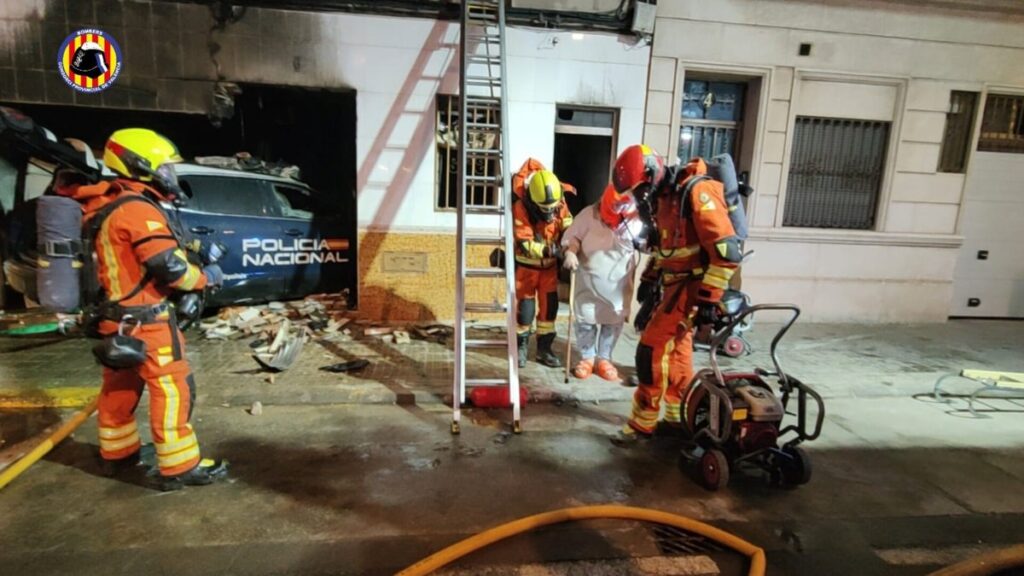 Fachada de vivienda destruida tras impacto de coche policial con humo y bomberos trabajando en Alaquàs