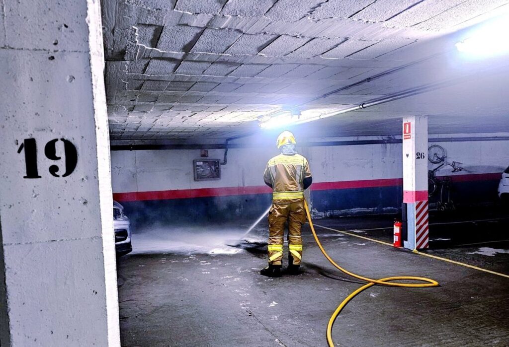 Bomberos extinguiendo llamas en garaje subterráneo con cartones quemados cerca de arqueta de ventilación