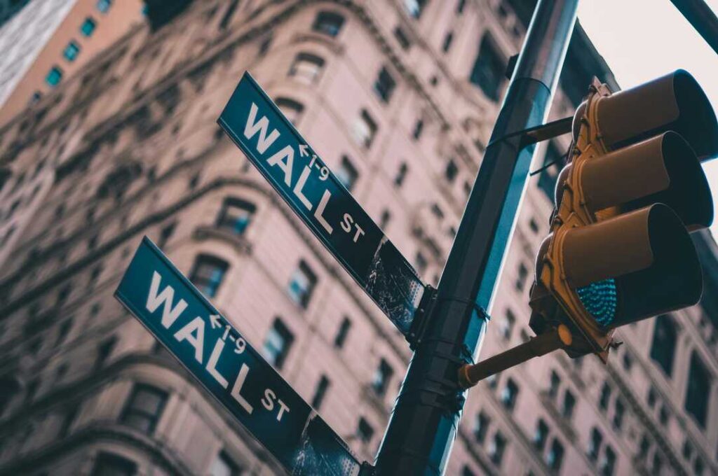 Pantallas de Wall Street mostrando el Dow Jones en rojo (-0,31%) con gráficos de caída por tensión Trump-China en tiempo real