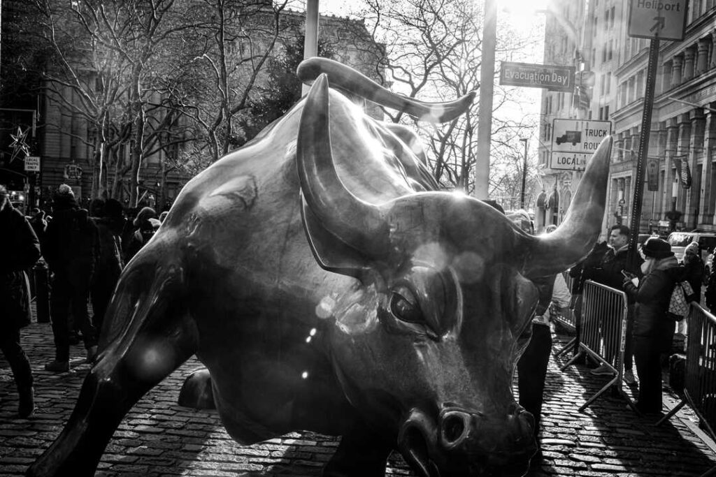 Periodista analizando datos en tiempo real desde el parqué del NYSE con pantallas de índices bursátiles al fondo