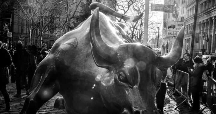 Periodista analizando datos en tiempo real desde el parqué del NYSE con pantallas de índices bursátiles al fondo