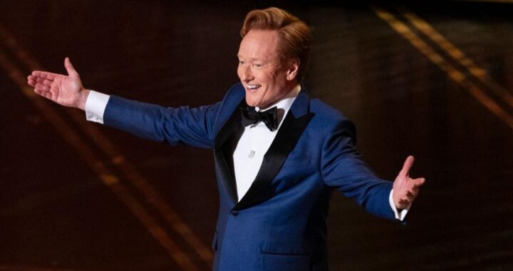Conan O'Brien sonríe en el escenario de los Oscar 2026 con fondo del Dolby Theatre, listo para su histórico tercer año como anfitrión en 2027