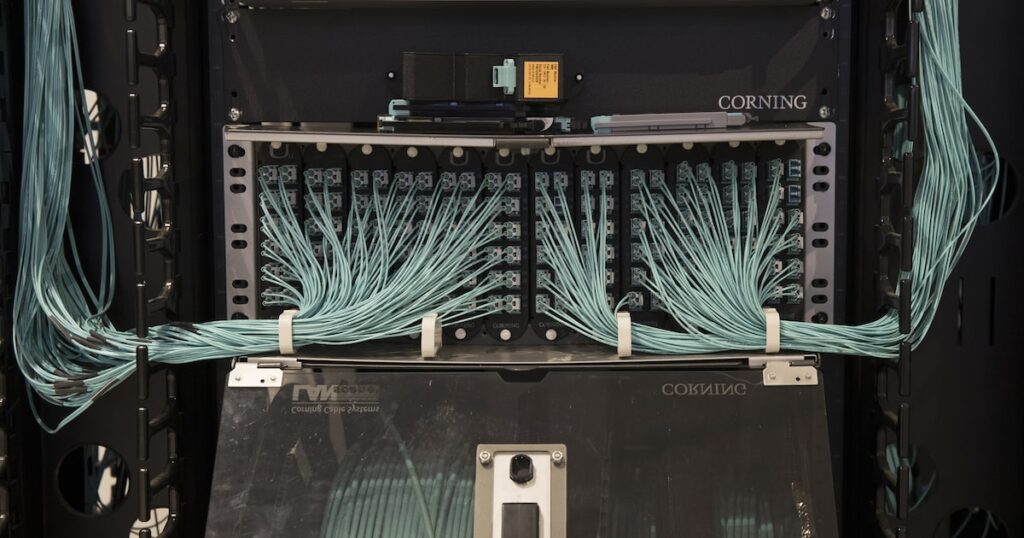 Gráfico de acciones de Corning con alza del 12,01% junto a logo de Nvidia y fibra óptica brillante