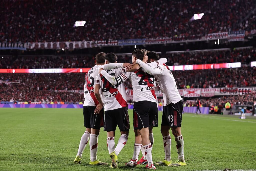 Gonzalo Montiel y Marcos Acuña lesionados en el banco de River, con rostros de preocupación y el equipo celebrando de fondo