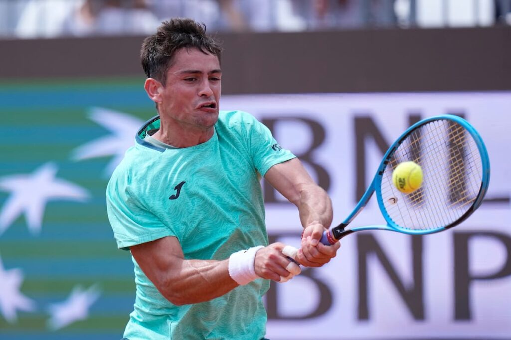 Mariano Navone agotado tras 3h02m de batalla en el court Pietrangeli de Roma, con Hamad Medjedovic celebrando al fondo entre estatuas de mármol