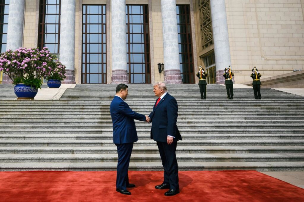 Trump y Xi Jinping sellan acuerdo con apretón de manos frente a banderas de EE.UU. y China, con mapa de Irán de fondo