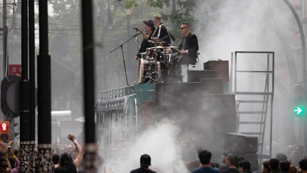 U2 en el techo de un autobús escolar con graffiti 'La calle de los sueños' en el Centro Histórico de CDMX, rodeados de fans