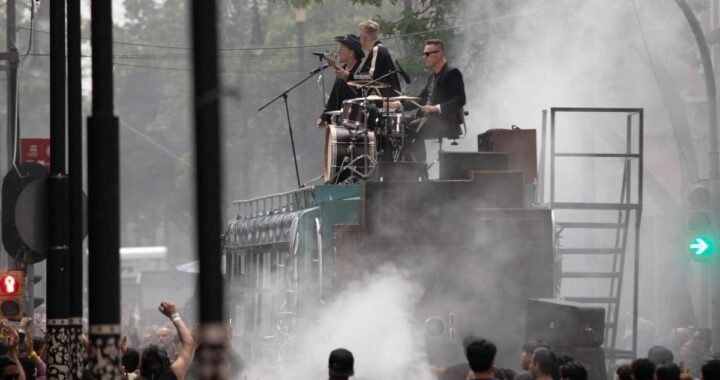 U2 en el techo de un autobús escolar con graffiti 'La calle de los sueños' en el Centro Histórico de CDMX, rodeados de fans