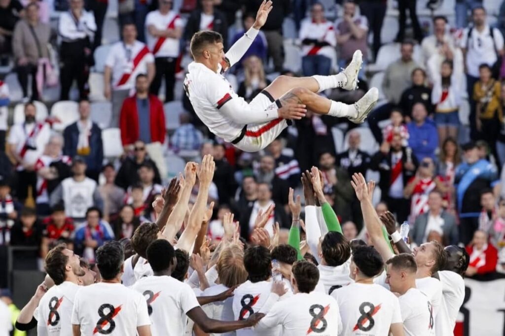 Óscar Trejo, capitán del Rayo Vallecano, levanta los brazos en Vallecas con el estadio de fondo y hinchas emocionados