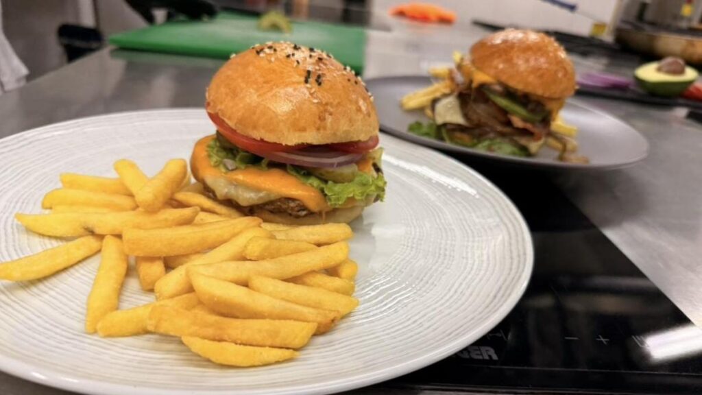 Chef aplastando carne en plancha para hamburguesa smash con queso derretido y costra dorada, técnica profesional