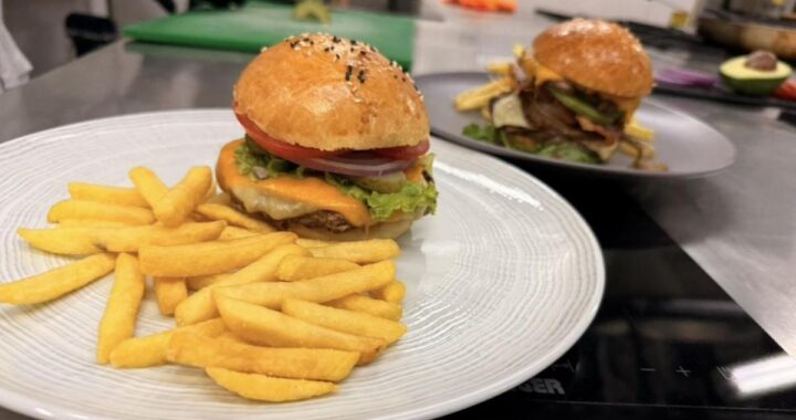 Chef aplastando carne en plancha para hamburguesa smash con queso derretido y costra dorada, técnica profesional