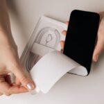 Manos sosteniendo un celular con etiqueta 'IMEI clonado' junto a un sello de Enacom tachado, alertando sobre contrabando