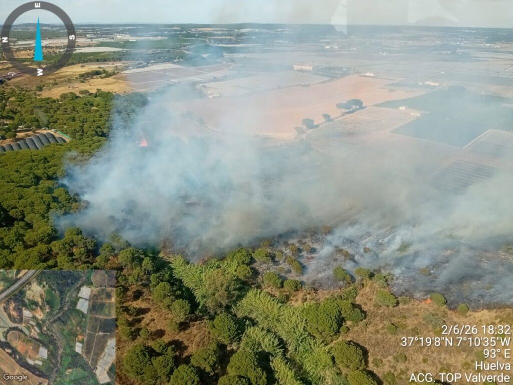 Helicóptero del Infoca con Bambi Bucket descargando agua sobre llamas en pinar de Huelva, con humo denso al fondo