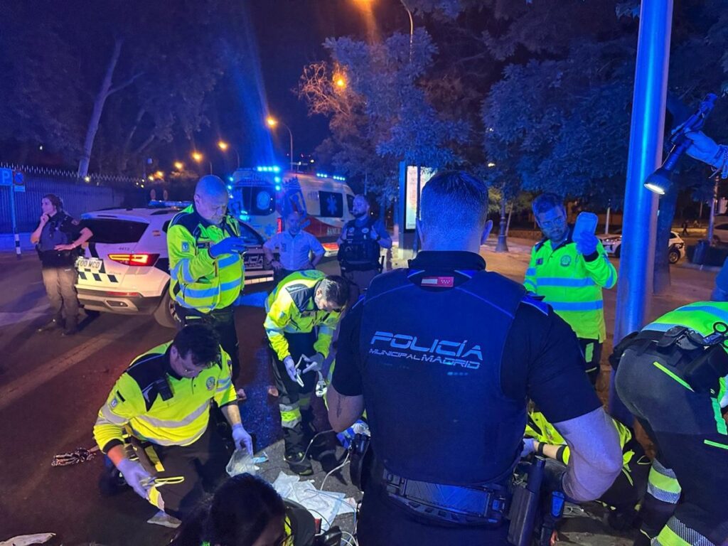 Motorista en el suelo tras caída nocturna en Paseo de la Castellana con ambulancia de fondo y luces de emergencia
