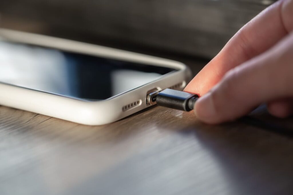 Cable USB conectado incorrectamente a un celular mostrando el riesgo de sobretensión en la batería